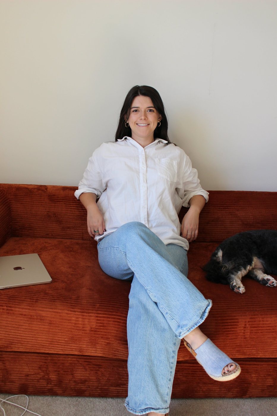 Elizabeth Craig, founder of Social Centre, sitting on a rust-coloured sofa with her dog and laptop